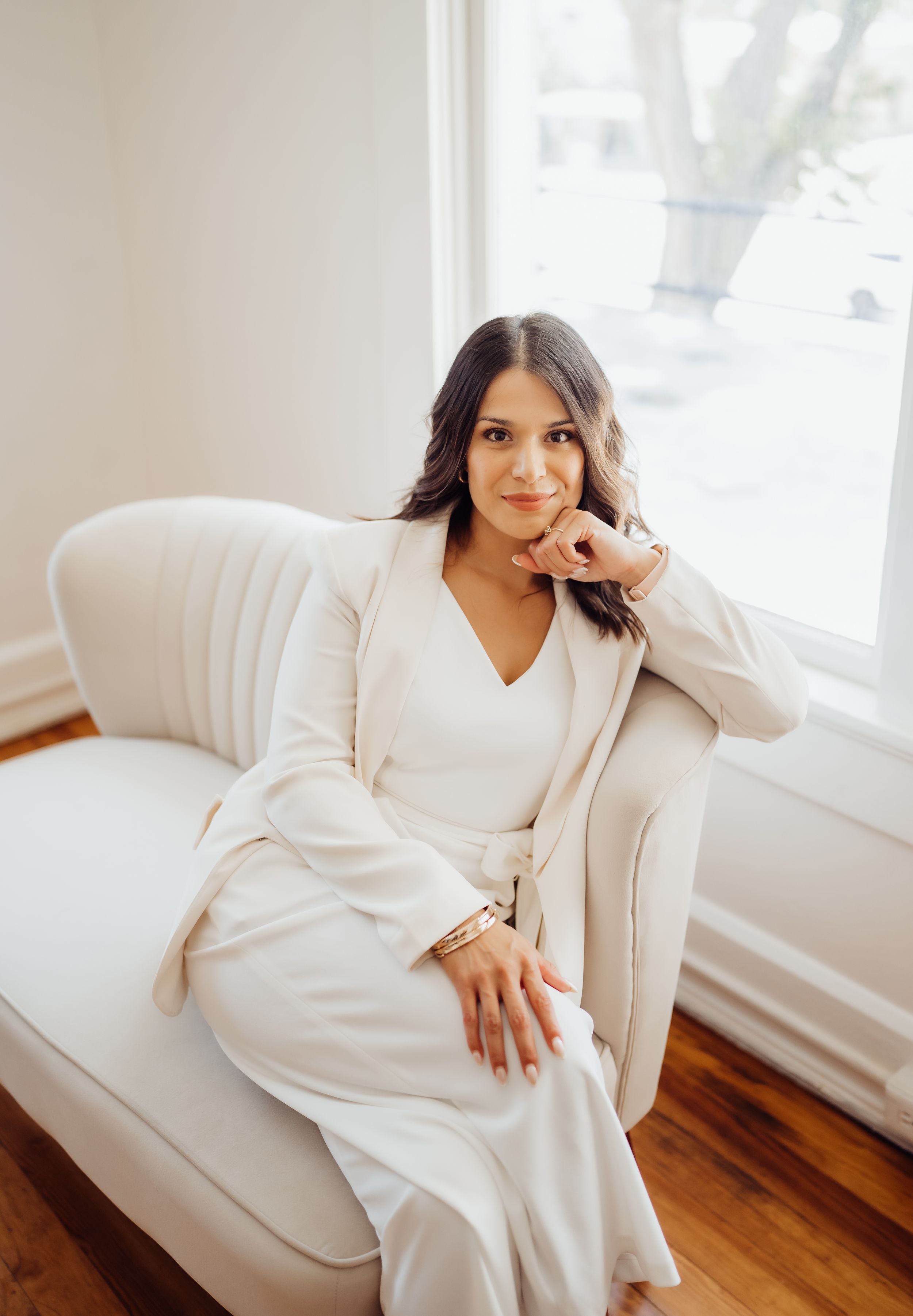 Casual portrait on cream sofa wearing monochromatic white outfit in sunlit room.