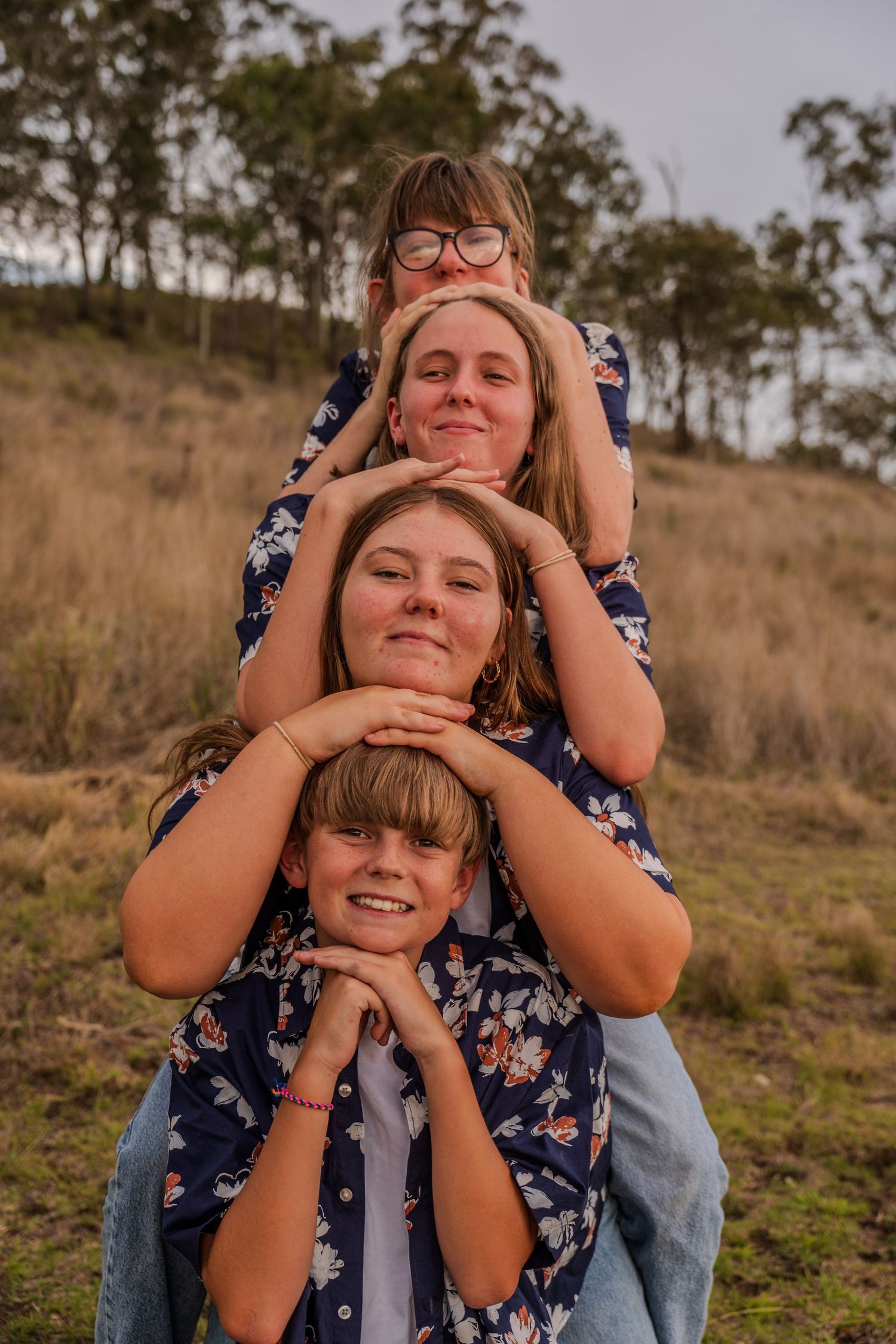 Four people stacked in a playful pose outdoors in matching floral outfits.