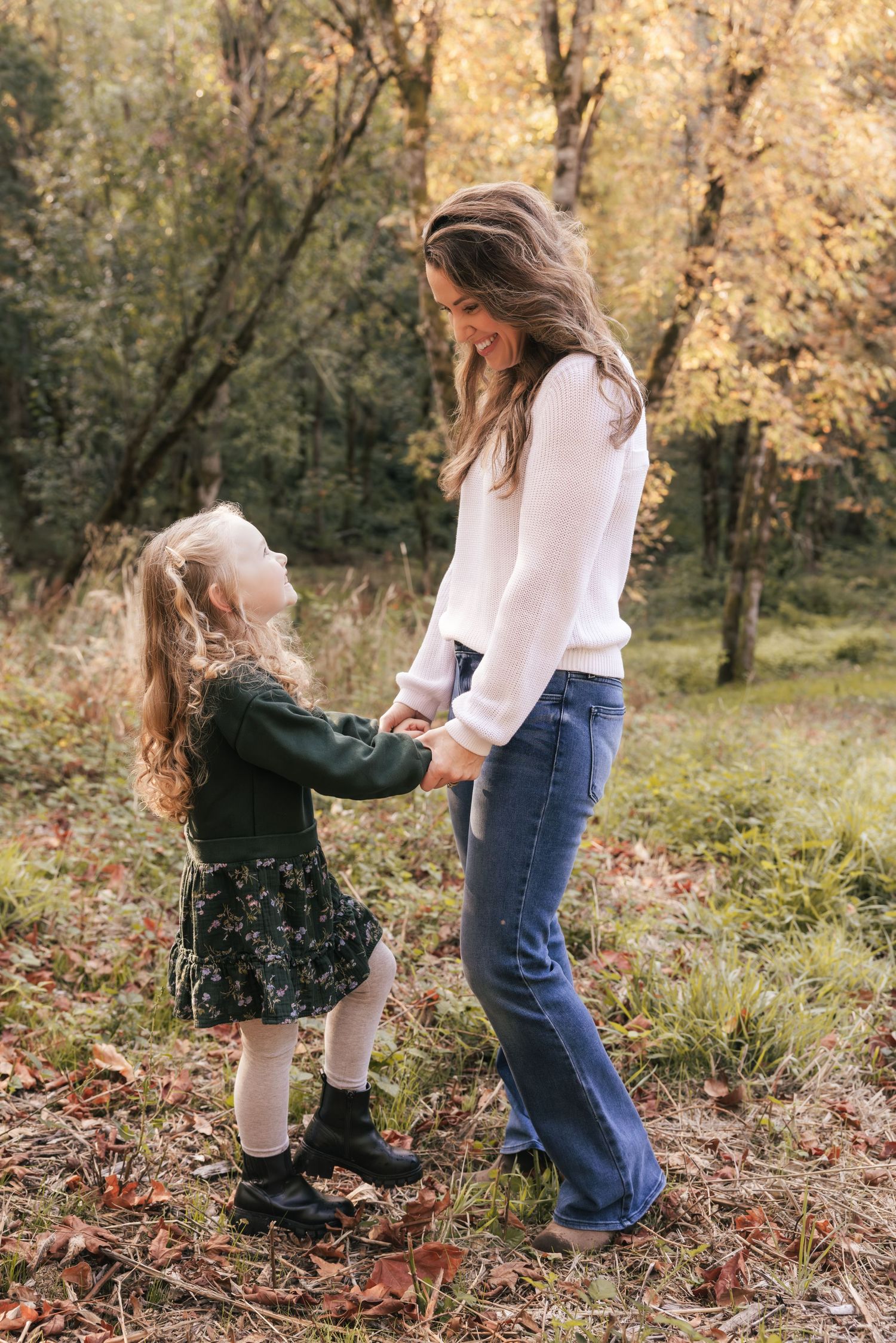 A parent and child hold hands and share a sweet moment together in an autumn forest setting with golden leaves.