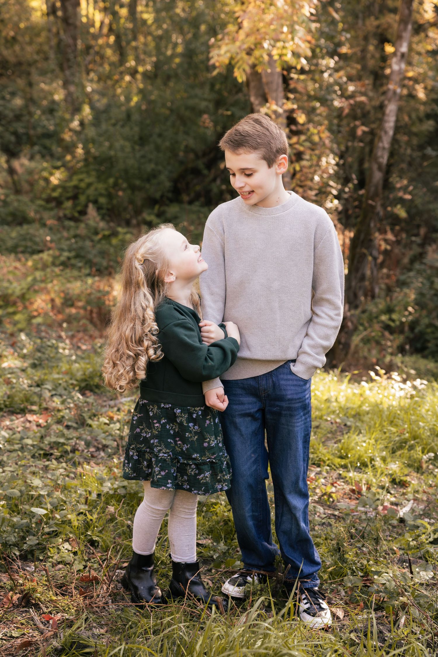Two siblings share a sweet moment outdoors in autumn with golden foliage in the background.
