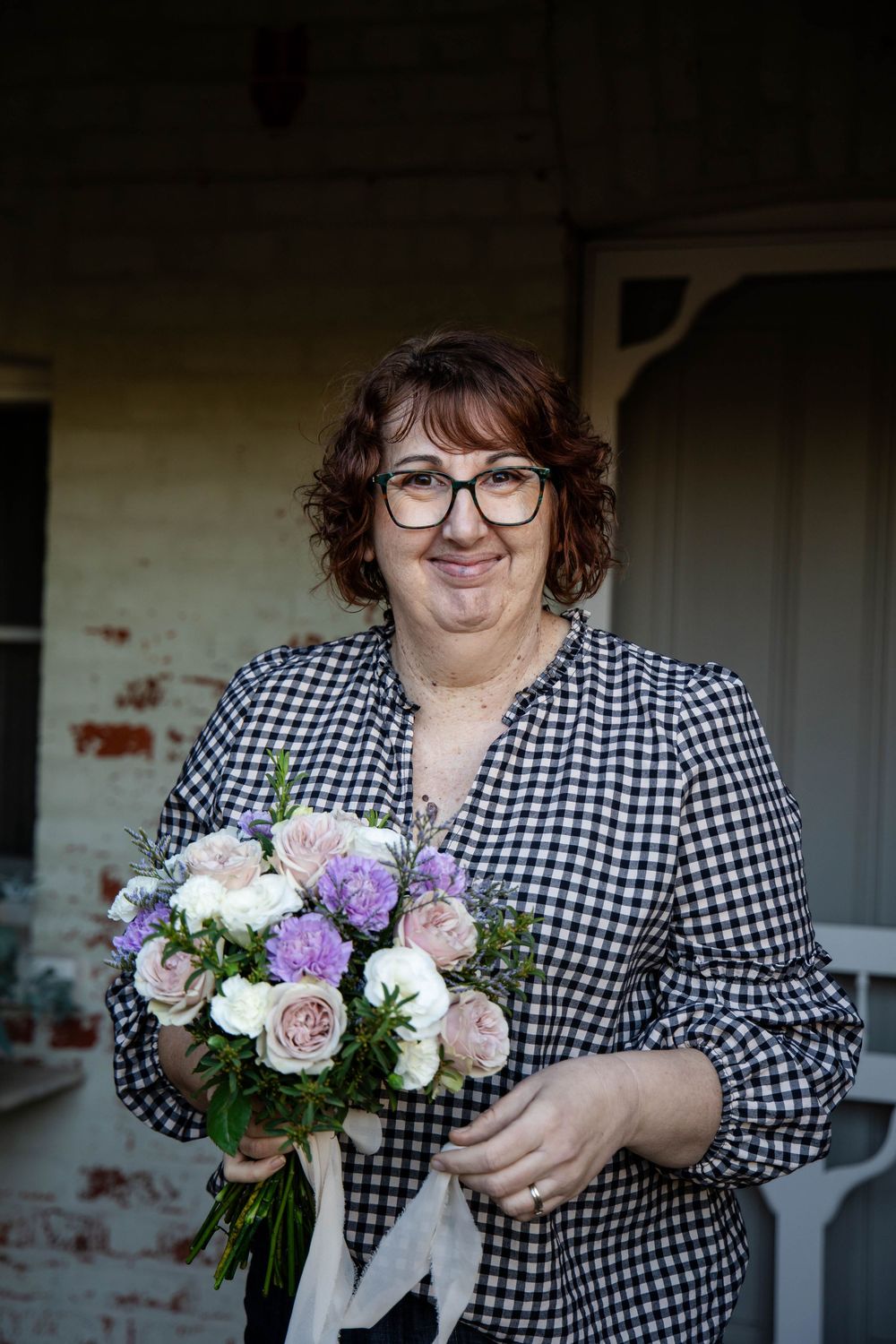 A person wearing a black and white gingham dress holds a soft pastel bouquet of pink and purple flowers.