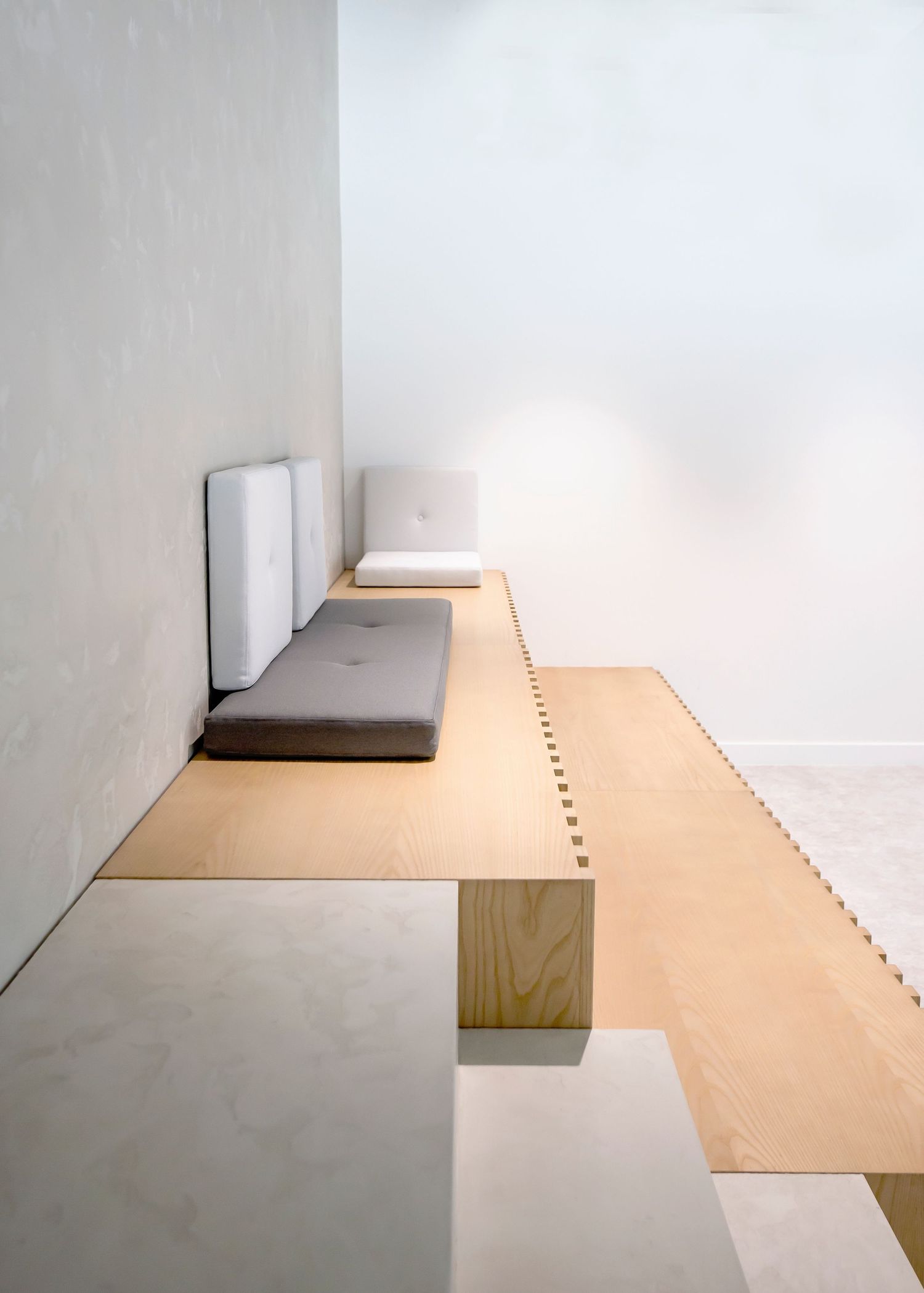 Minimalist interior featuring a floating wooden bench with gray cushions against white walls on a light wooden floor.