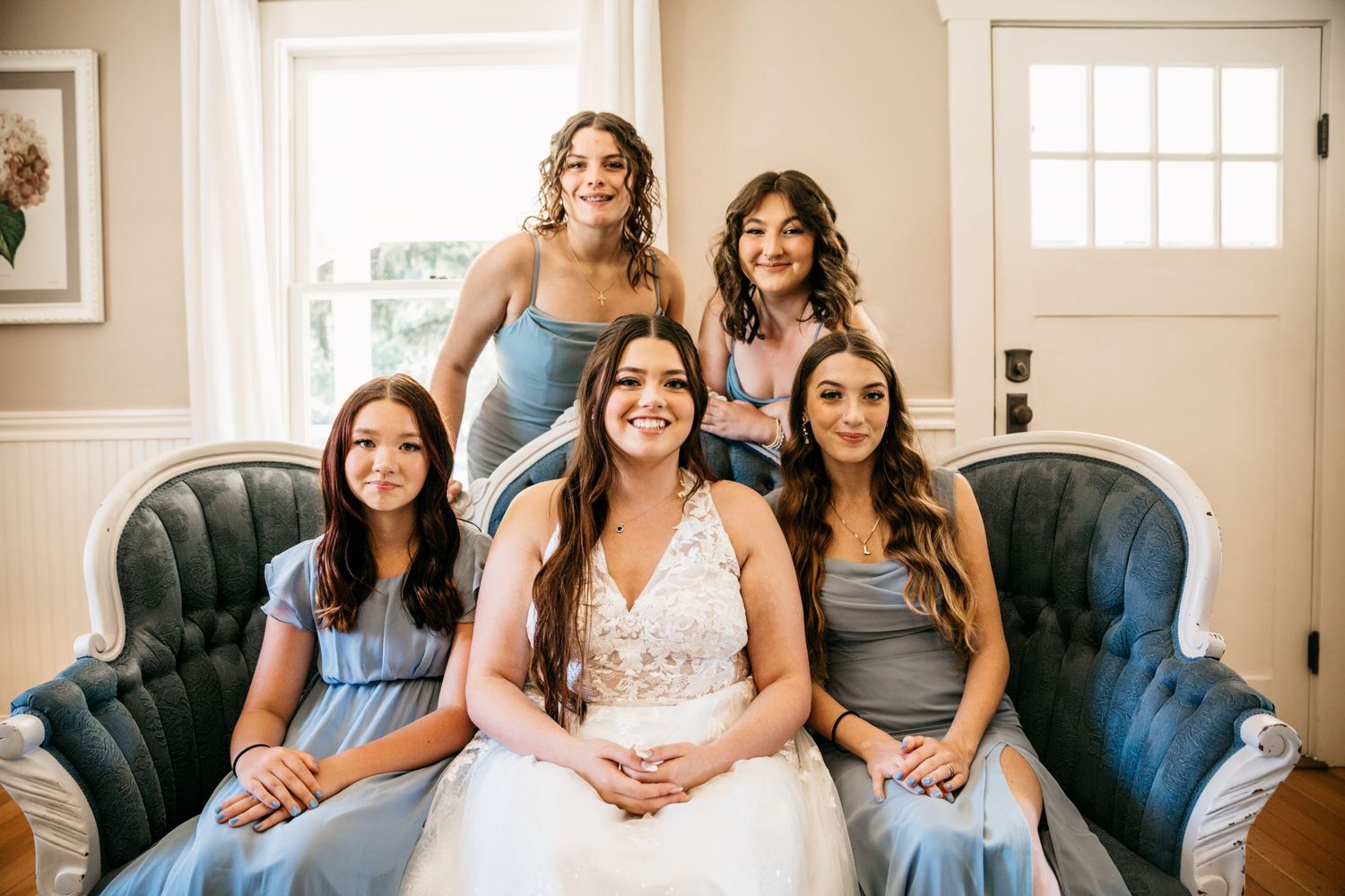 Bridal party relaxing on vintage blue sofa in elegant indoor setting.