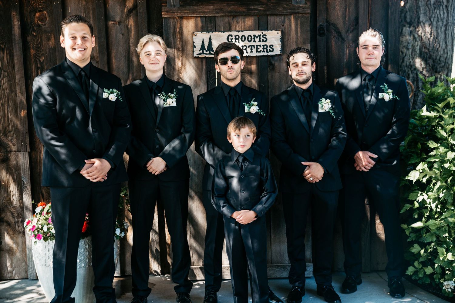Groomsmen and young ring bearer in matching black suits pose for formal photo.