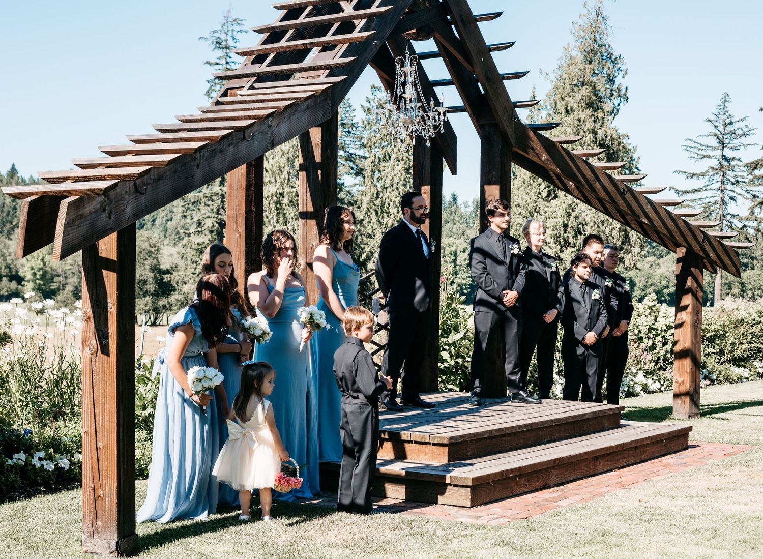 Wedding ceremony taking place under a rustic wooden arch structure with guests gathered around.
