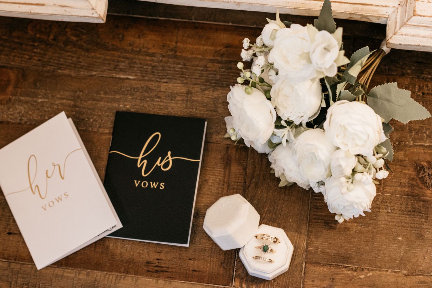 Wedding vow books and ring box arranged with white roses on wooden surface.