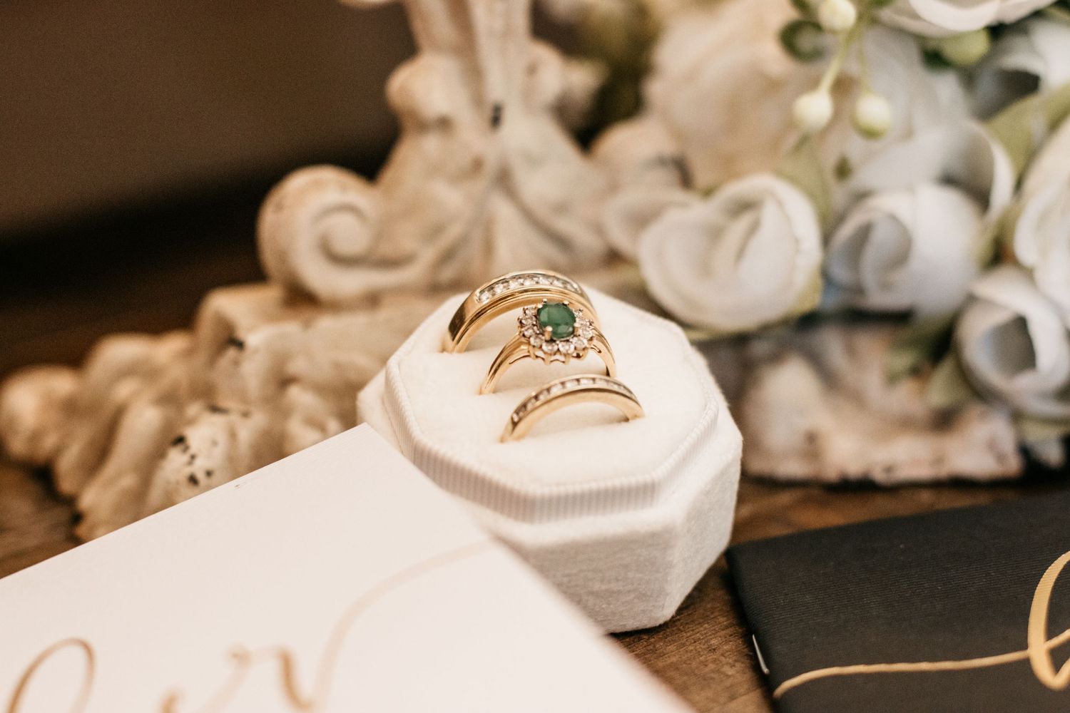 Wedding rings displayed on a white cushion with floral decorations in the background.