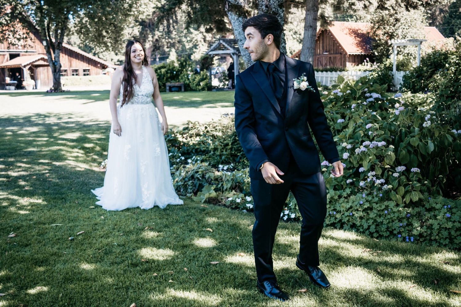 A wedding couple poses in a garden setting with lush greenery and trees in the background.