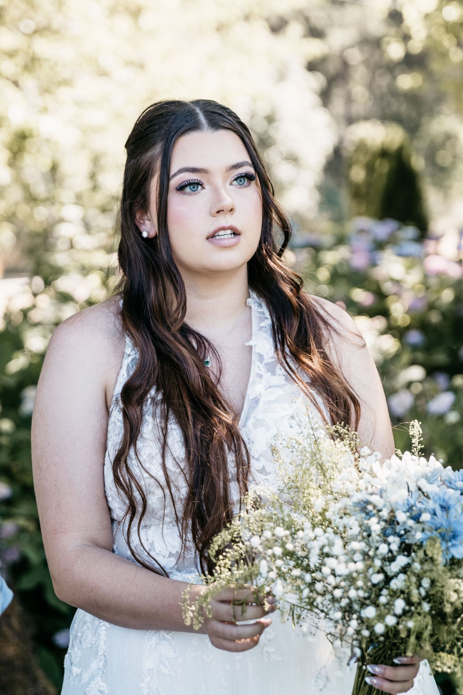 The bride holds a delicate bouquet of baby's breath flowers while wearing a detailed lace wedding gown.