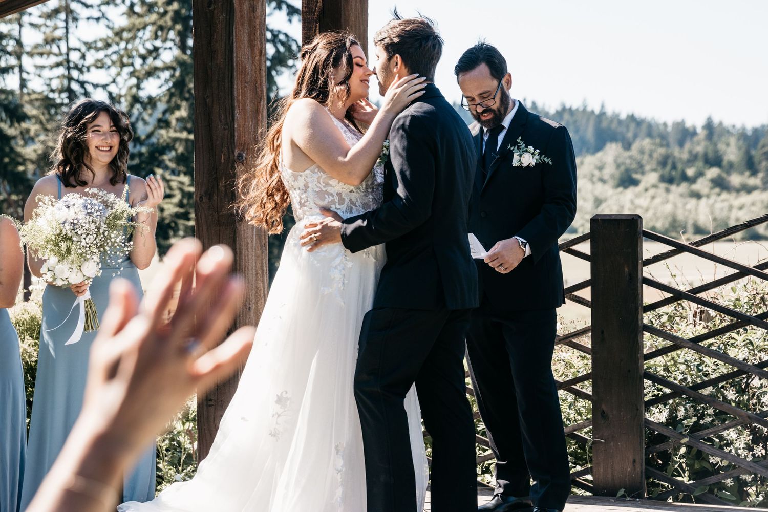 An outdoor wedding ceremony with guests watching the couple exchange vows under a wooden pergola.