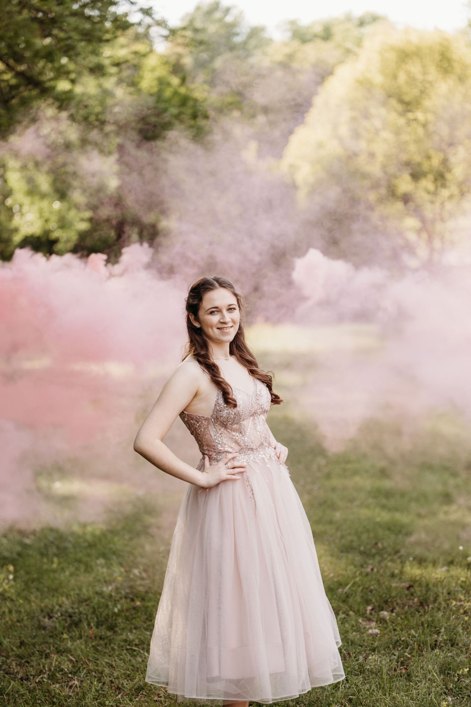 Ethereal portrait in a garden with pink smoke effects and a flowing tulle dress in soft natural lighting.