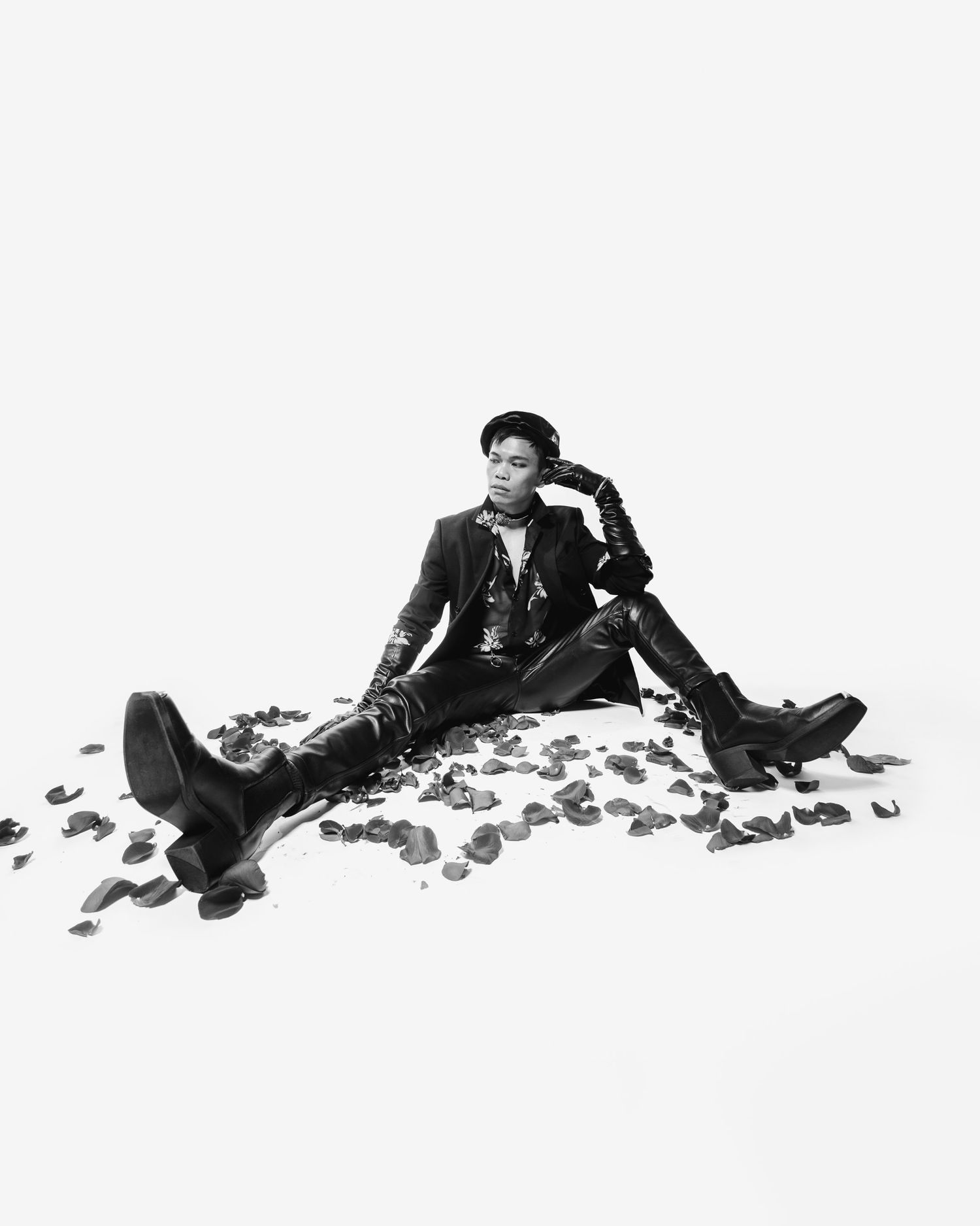 Black and white artistic portrait of someone relaxed on the ground surrounded by scattered petals wearing leather jacket.
