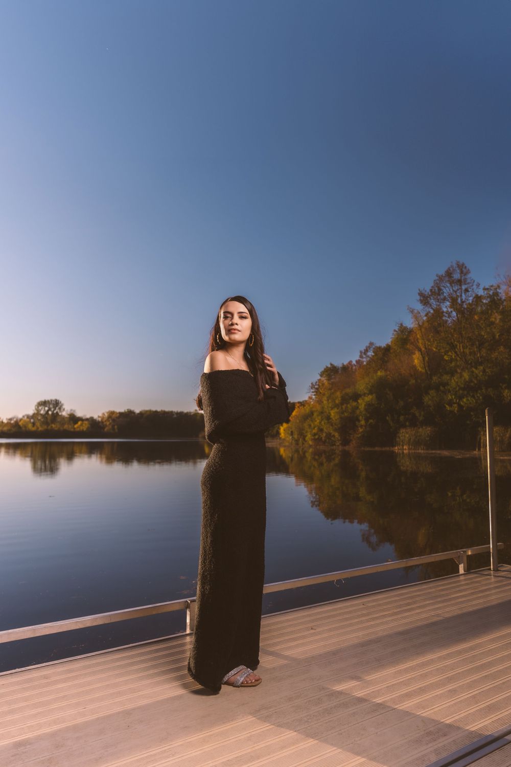 A silhouette stands on a wooden dock overlooking a serene lake during sunset.
