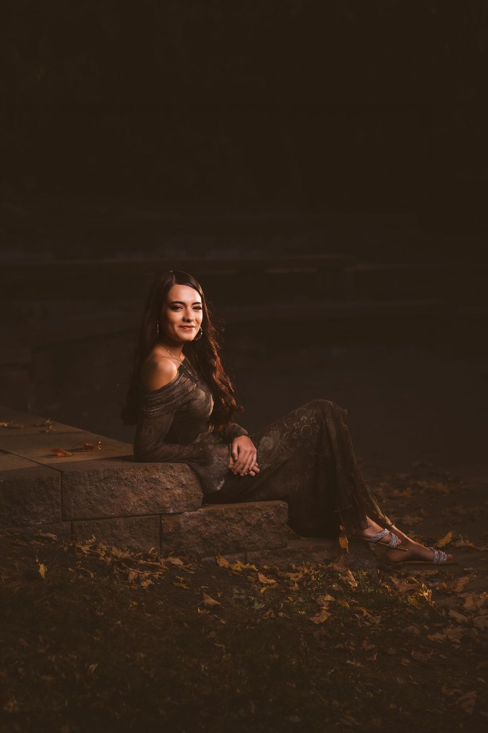A person in dark clothing sits on rocky terrain in dramatic low-key lighting.