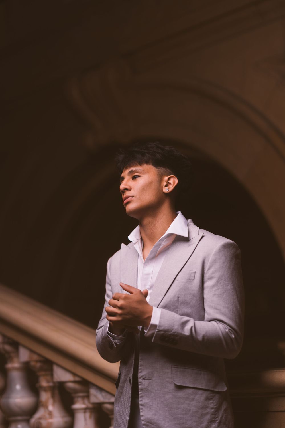 A person in a gray blazer stands in front of an architectural archway with dramatic lighting.