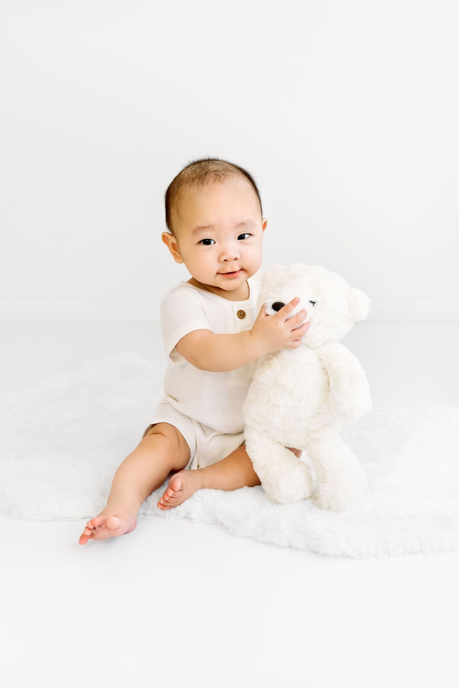7 Month old boy portrait, simple white background, holding white teddy bear.