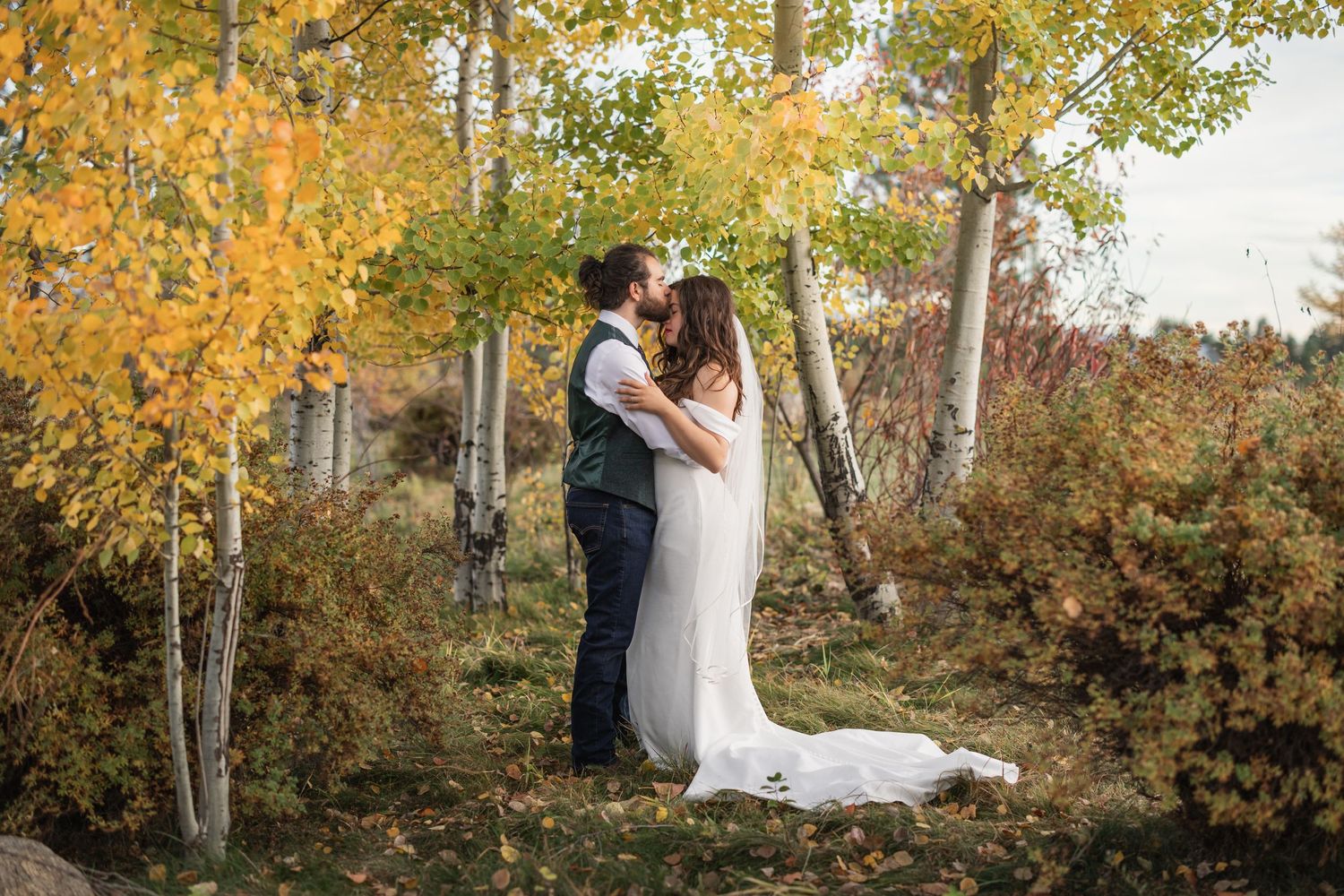 A wedding couple shares an intimate moment among golden aspen trees in autumn.