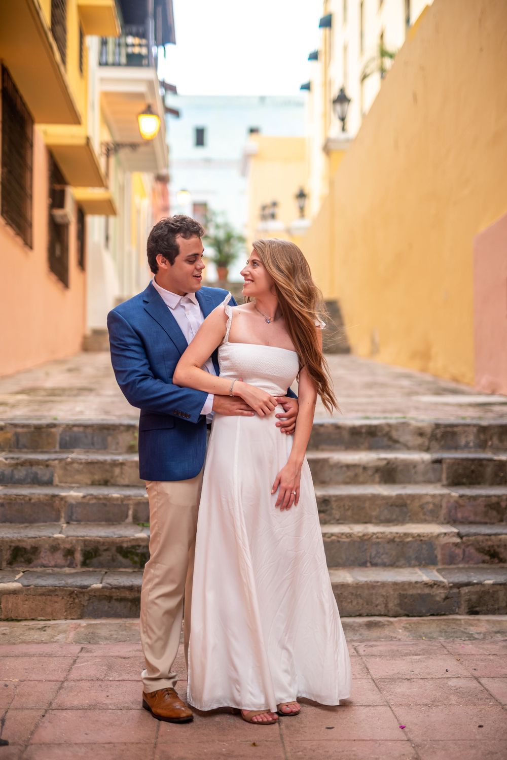 Romantic couple posing on yellow-walled steps in tropical setting.