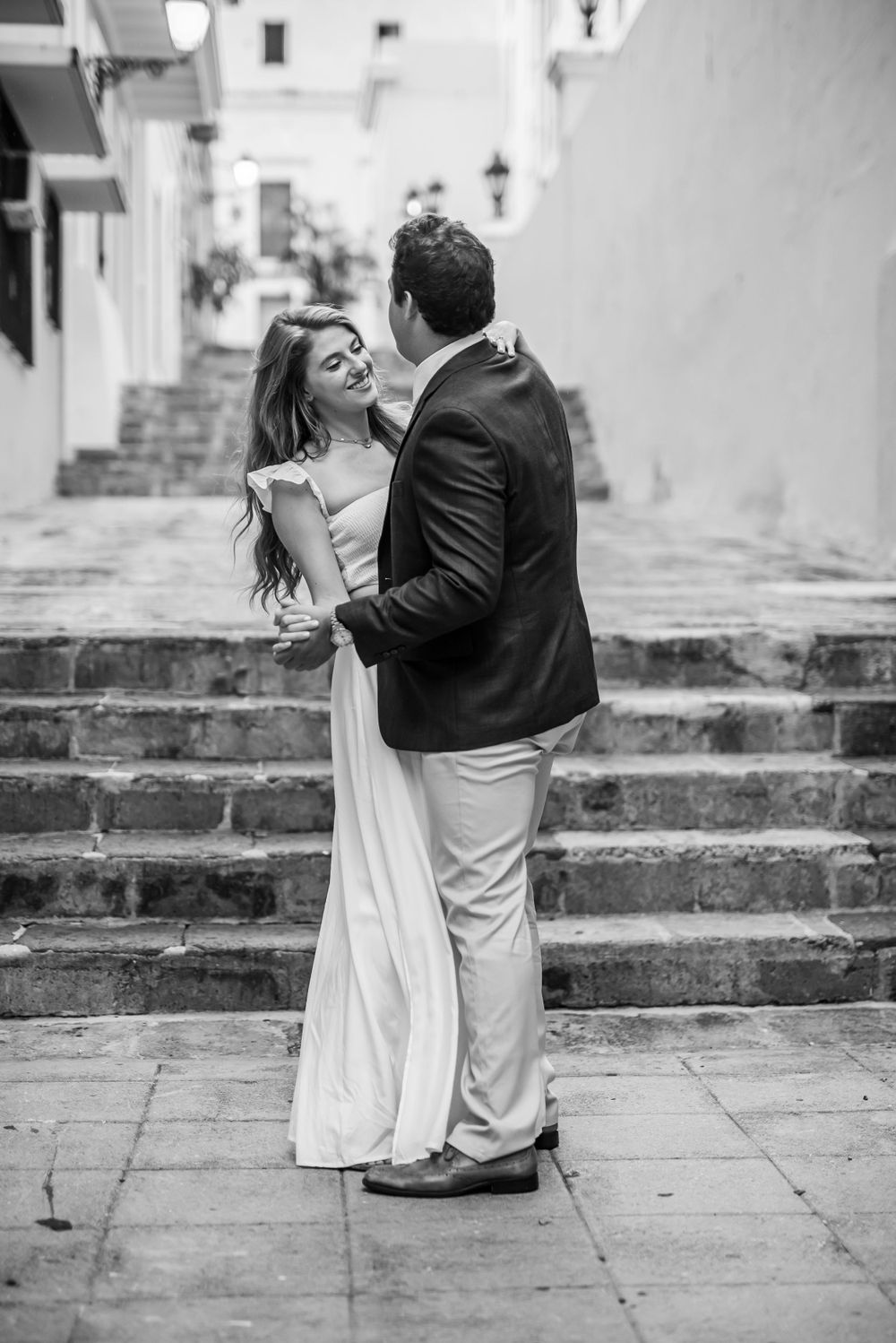 A black and white portrait of a couple embracing on historic stone steps.