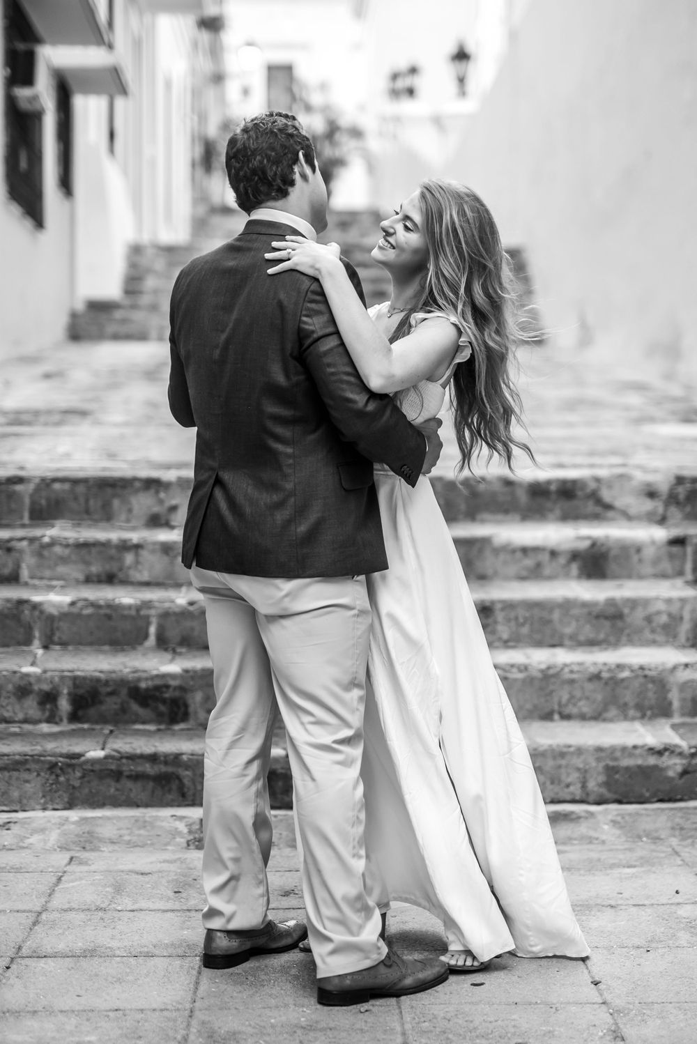 A couple sharing an intimate dance moment on stone steps in a monochrome setting.