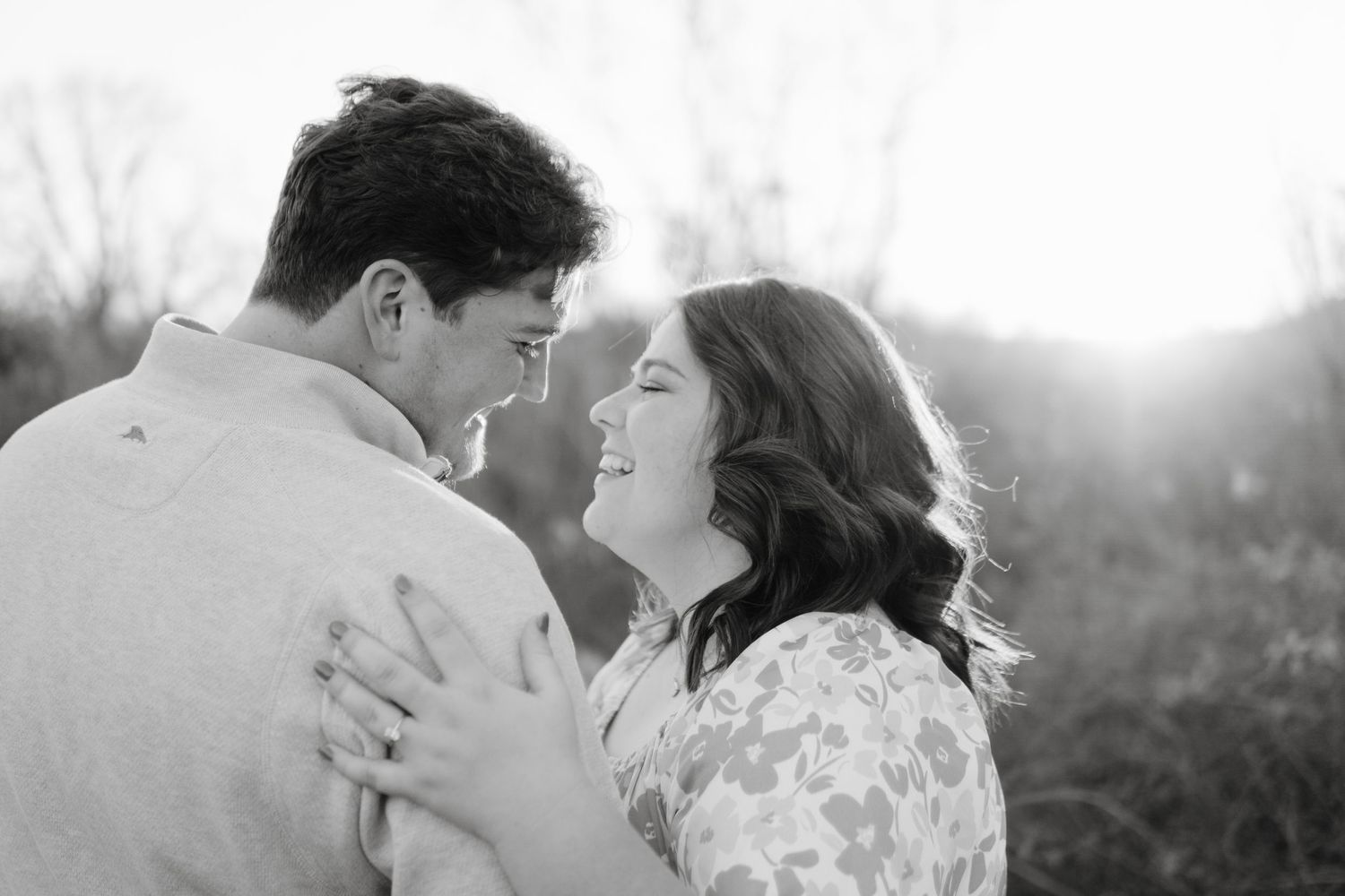 A romantic black and white portrait of a couple embracing outdoors in soft sunlight.
