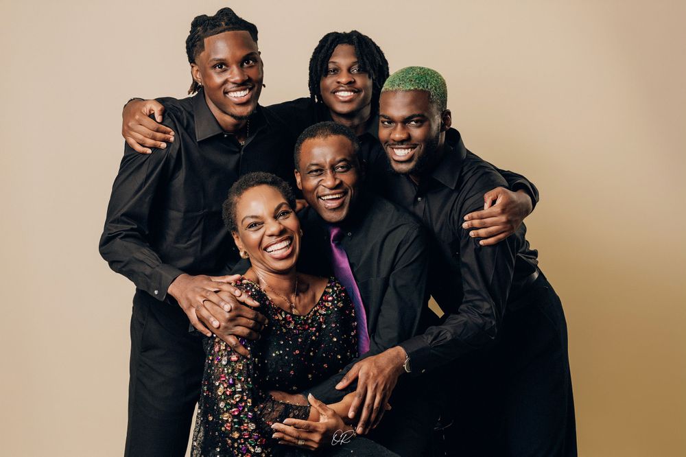 Group studio portrait featuring coordinated black outfits against neutral background.