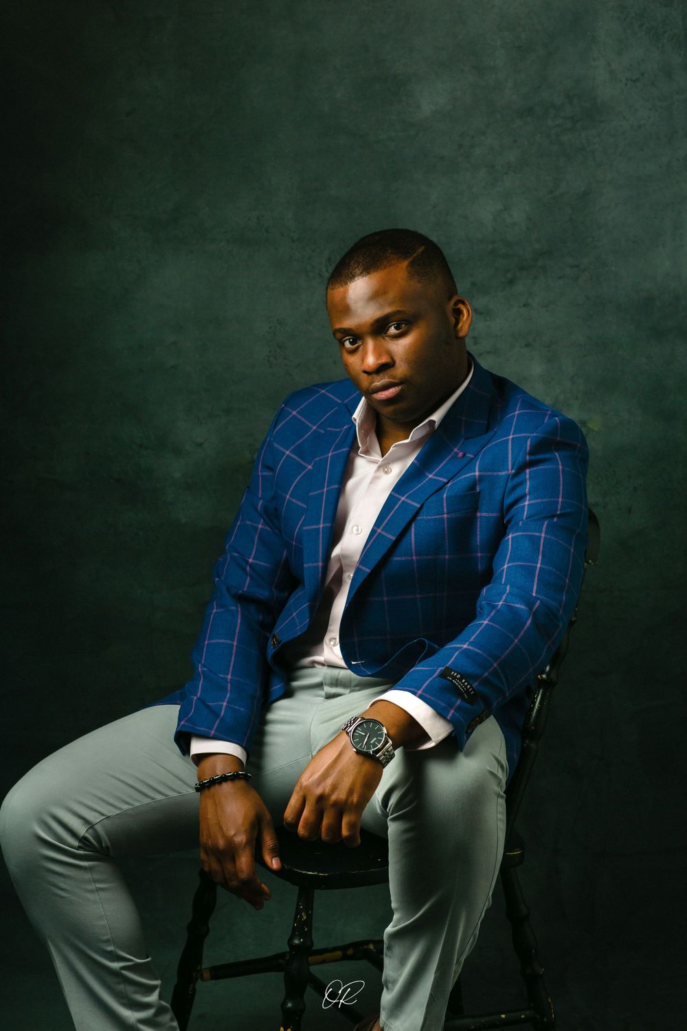 Professional portrait in blue checkered blazer against dark green textured background.