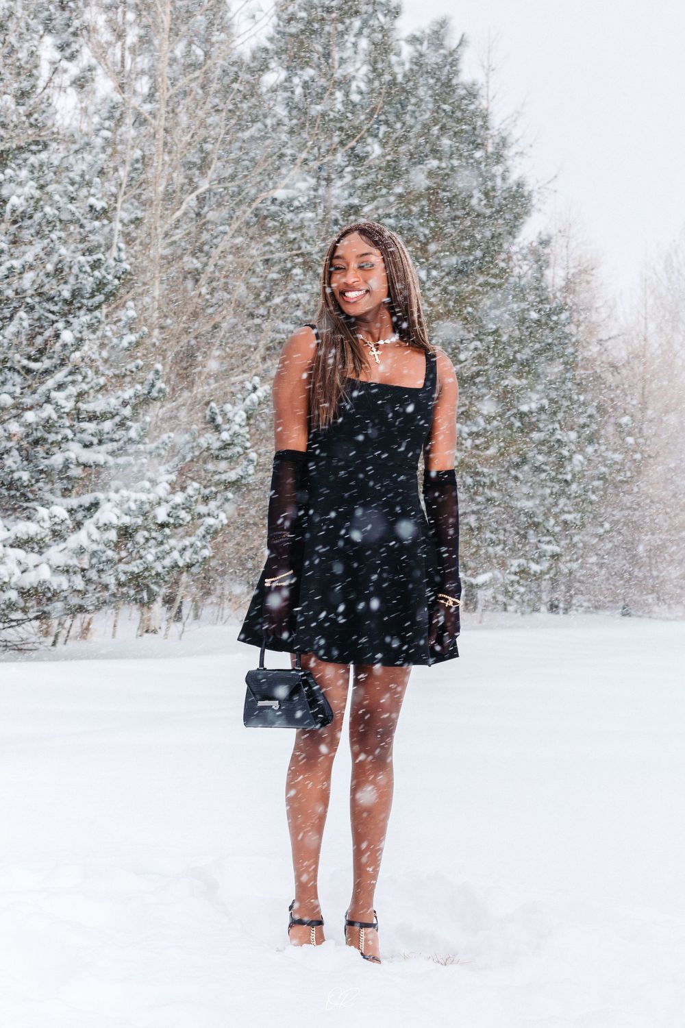 Winter fashion portrait in falling snow featuring black dress and accessories.
