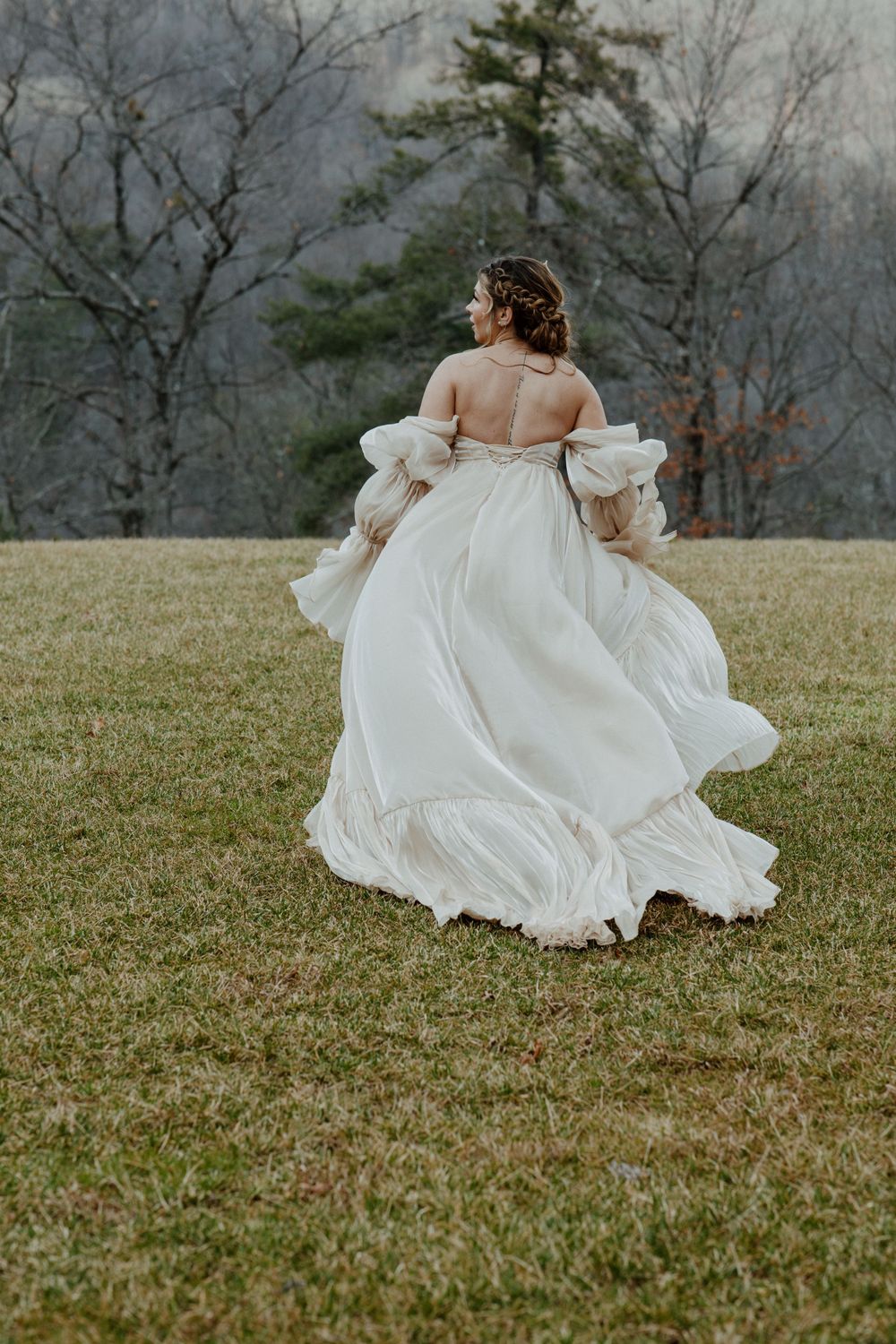 Off-shoulder white wedding dress flowing in motion on a grassy hillside.