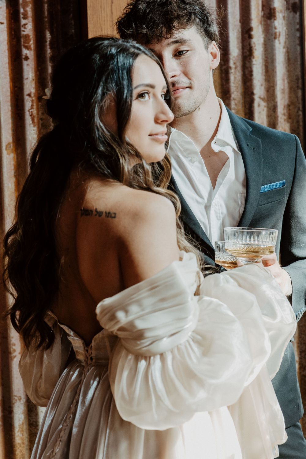 Intimate wedding portrait with couple embracing while holding cocktail glass.