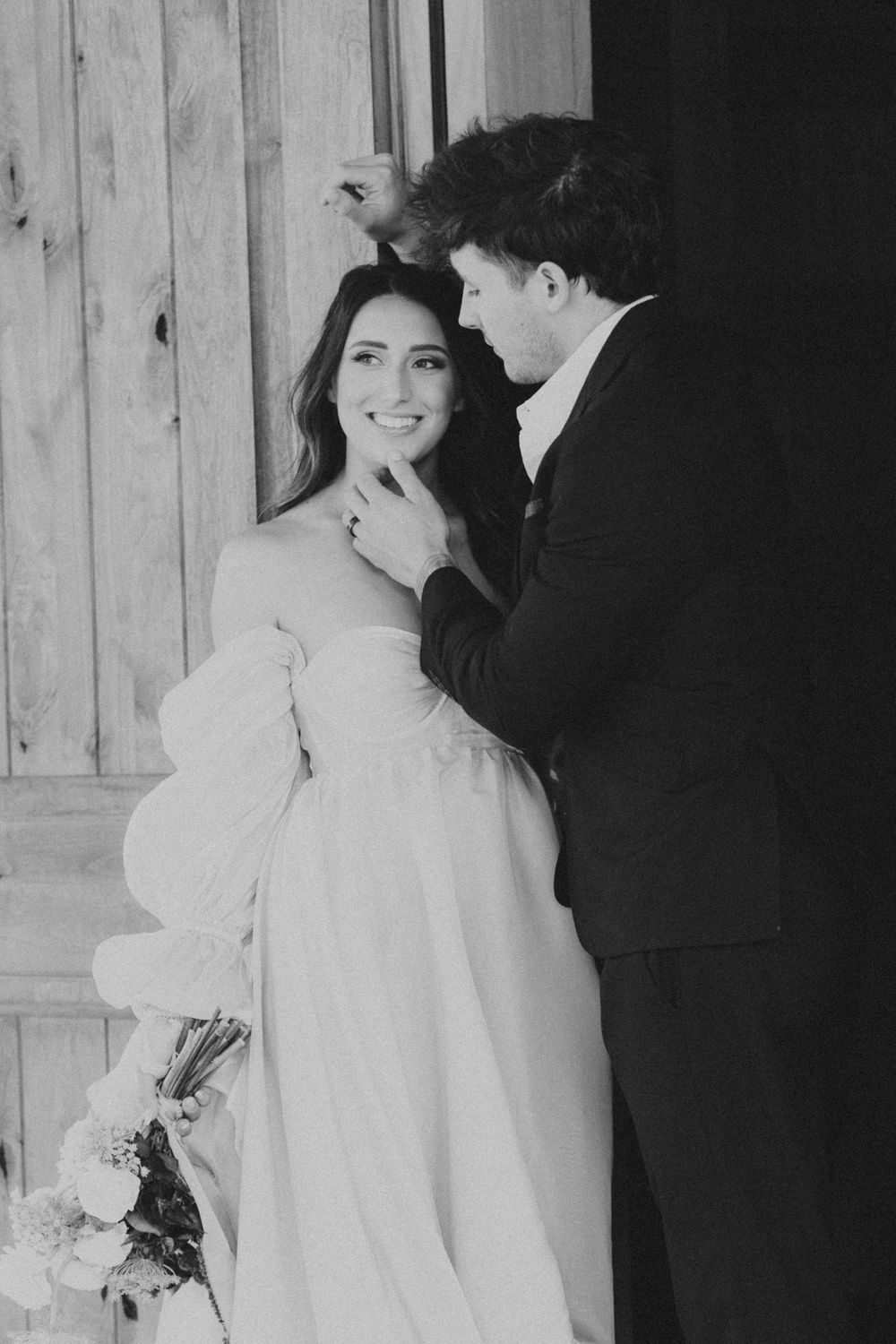 Black and white intimate wedding portrait against a rustic wooden backdrop.