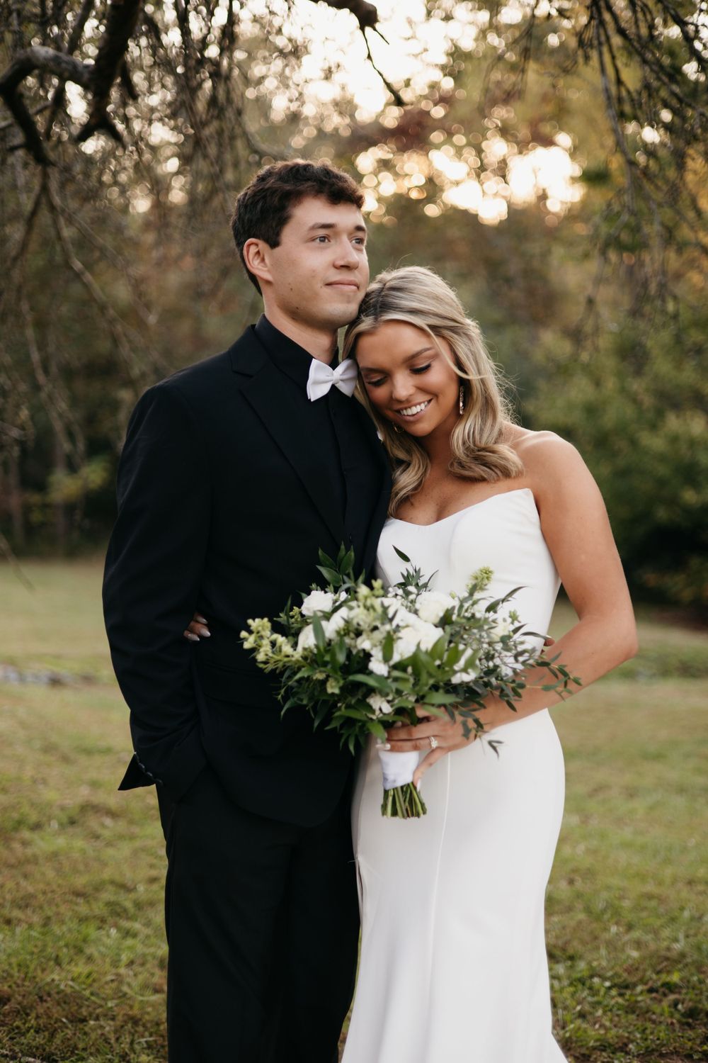 Romantic portrait of newlyweds embracing with white bouquet during golden hour.