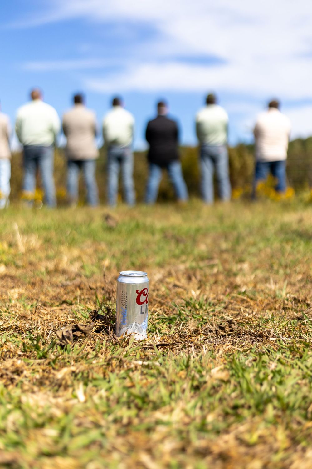 Beer can in foreground with groomsmen standing in distance on grassy hill.