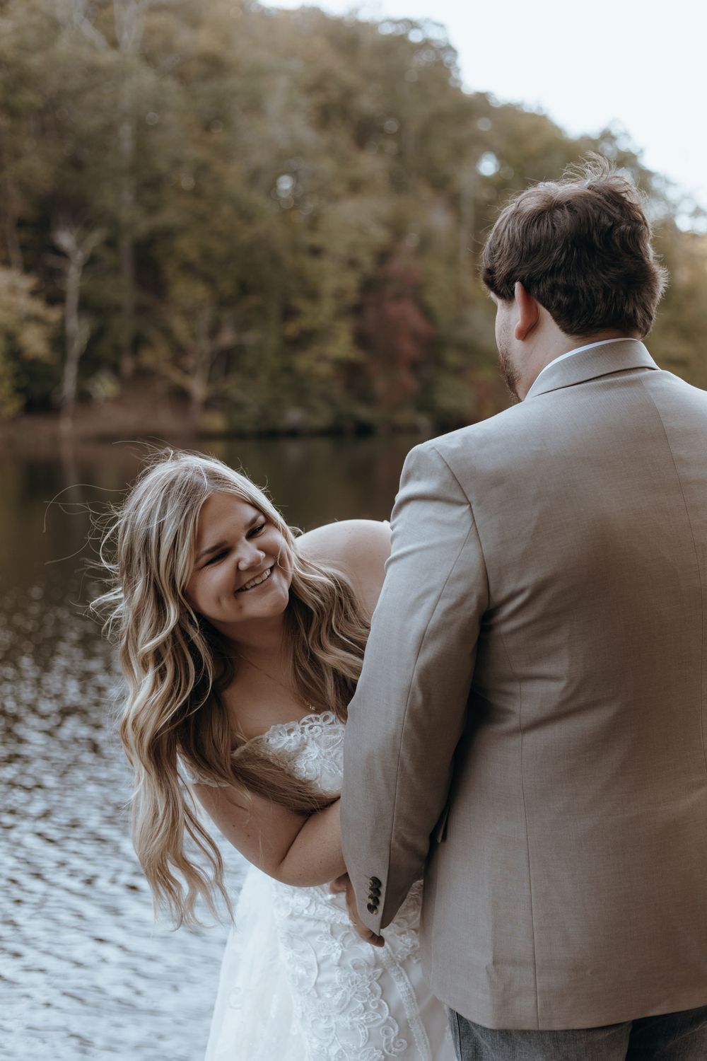 Bride and groom share intimate moment by lakeside during wedding photoshoot.