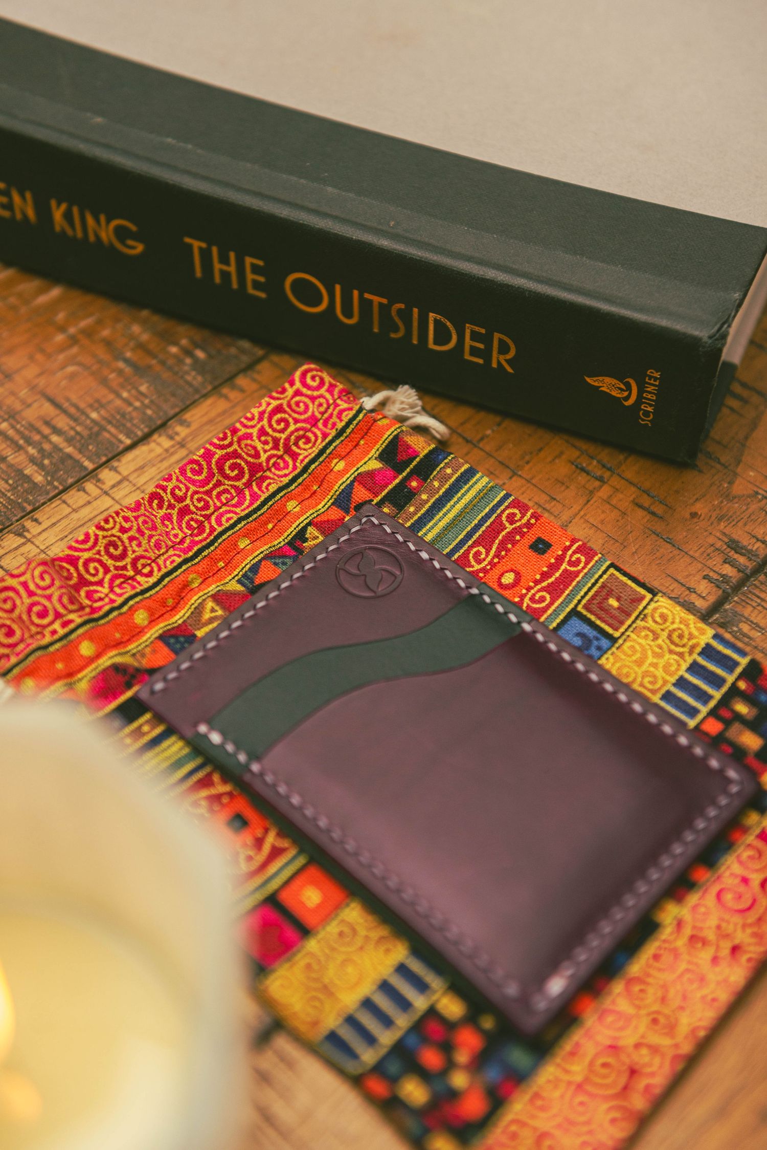 Stephen King book 'The Outsider' with leather wallet on colorful patterned fabric.