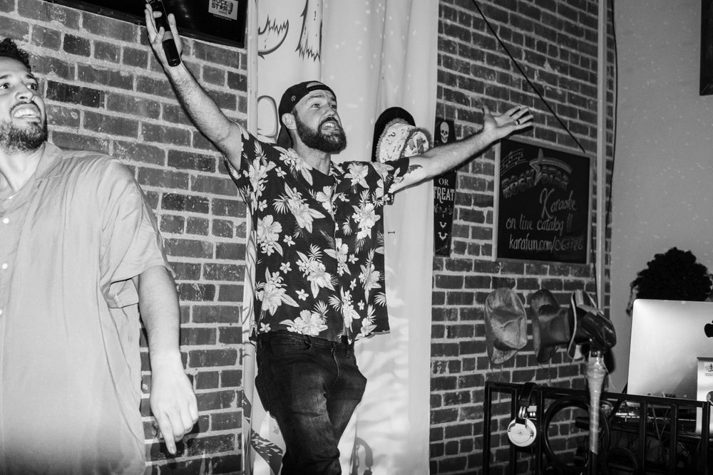 Black and white photo of people celebrating with raised arms against a brick wall background.