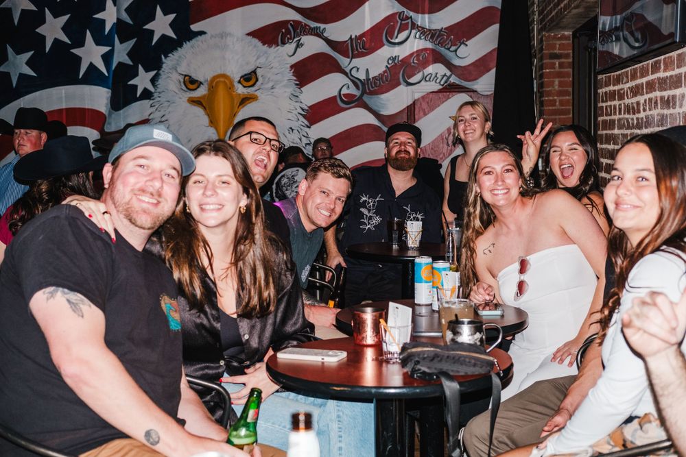 Group gathered around a table at a bar with American flag decor in the background.