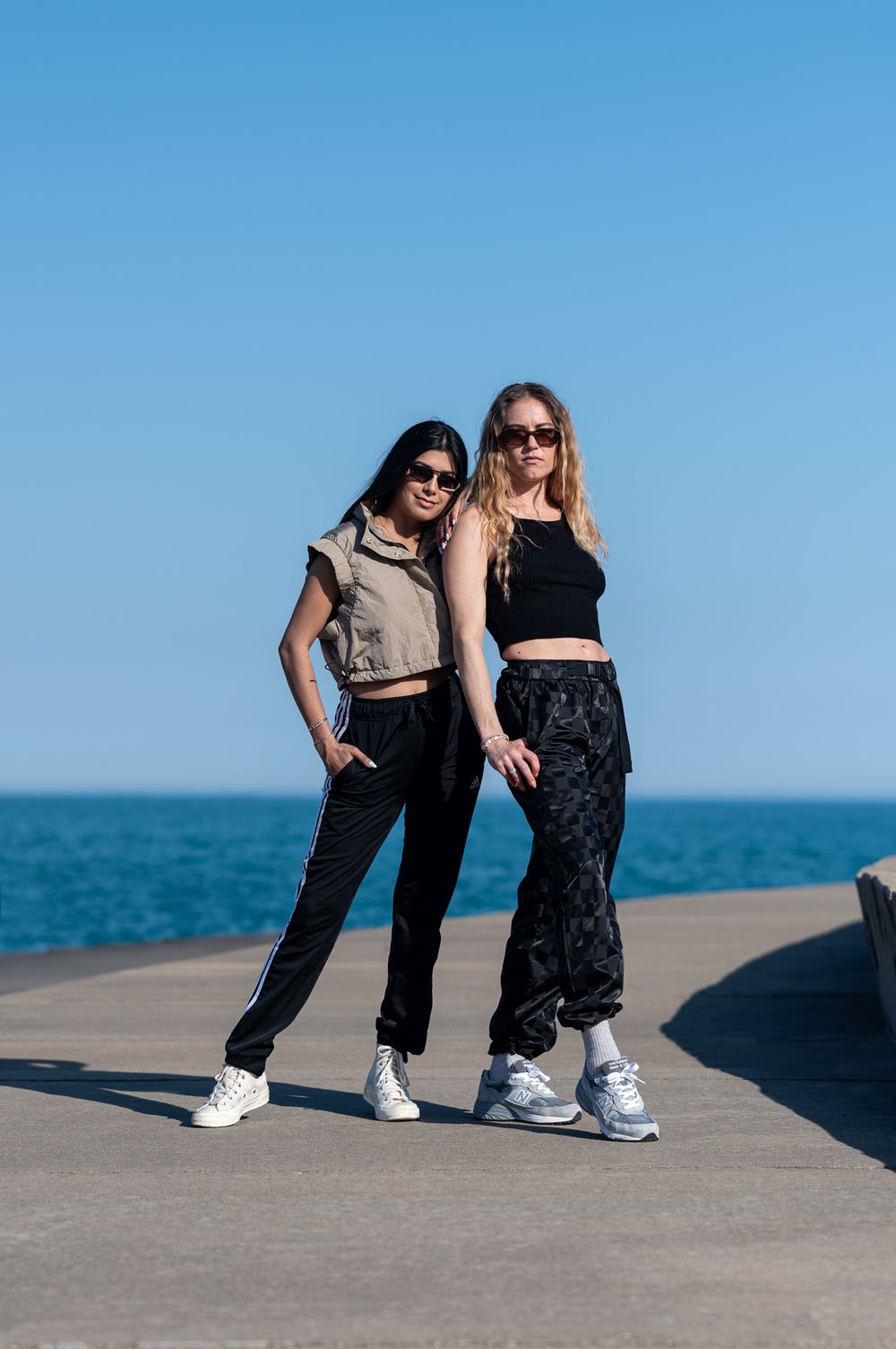 Two friends in athletic wear pose together on a pier with a body of water behind them.