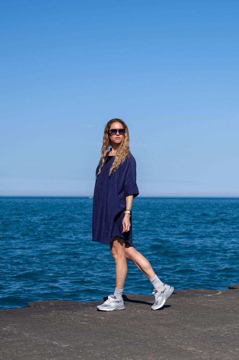 Fashion shot of person in flowing navy dress and sneakers by a body of water.