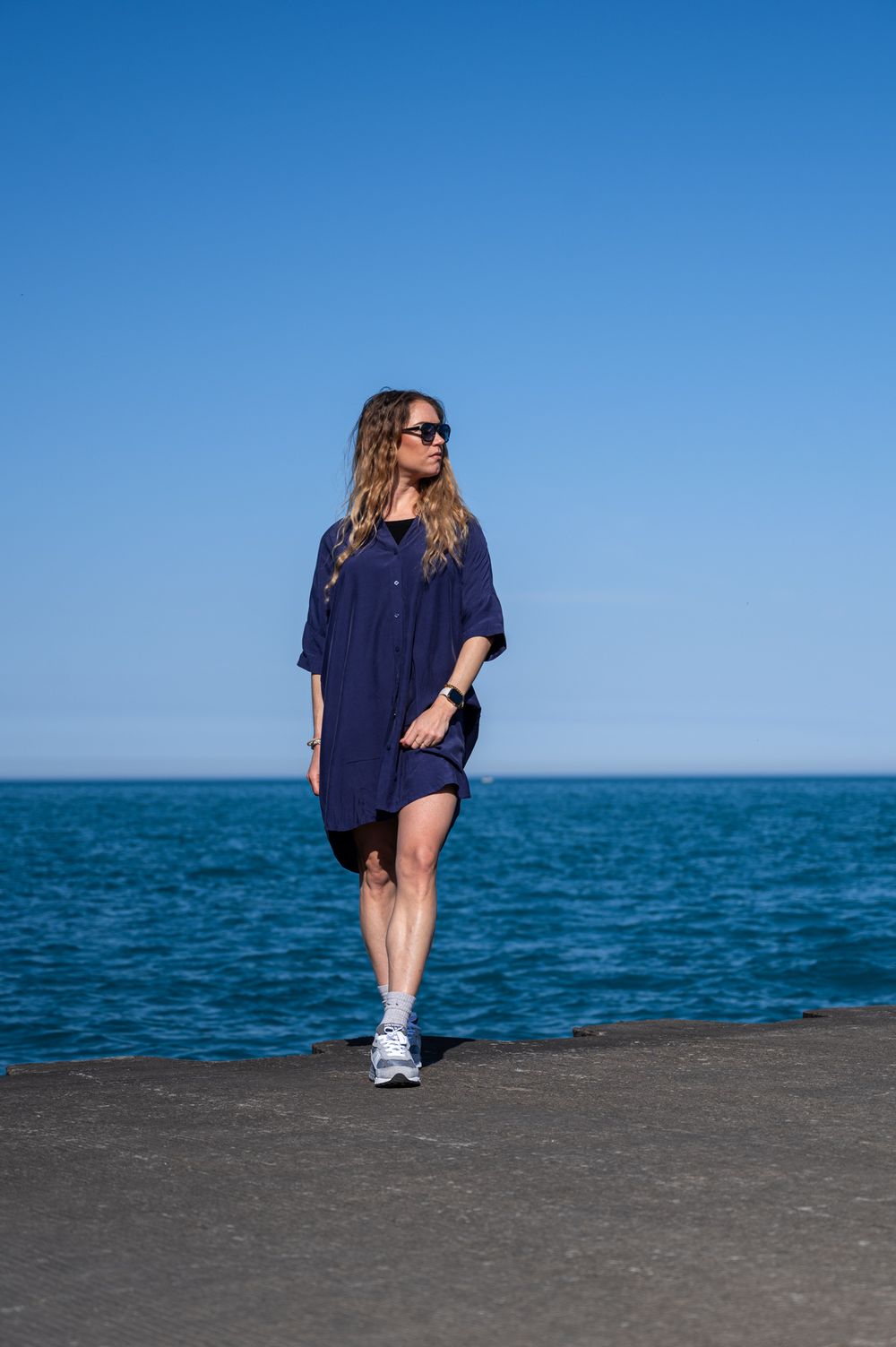 Person in navy dress walking along water front on a sunny day.