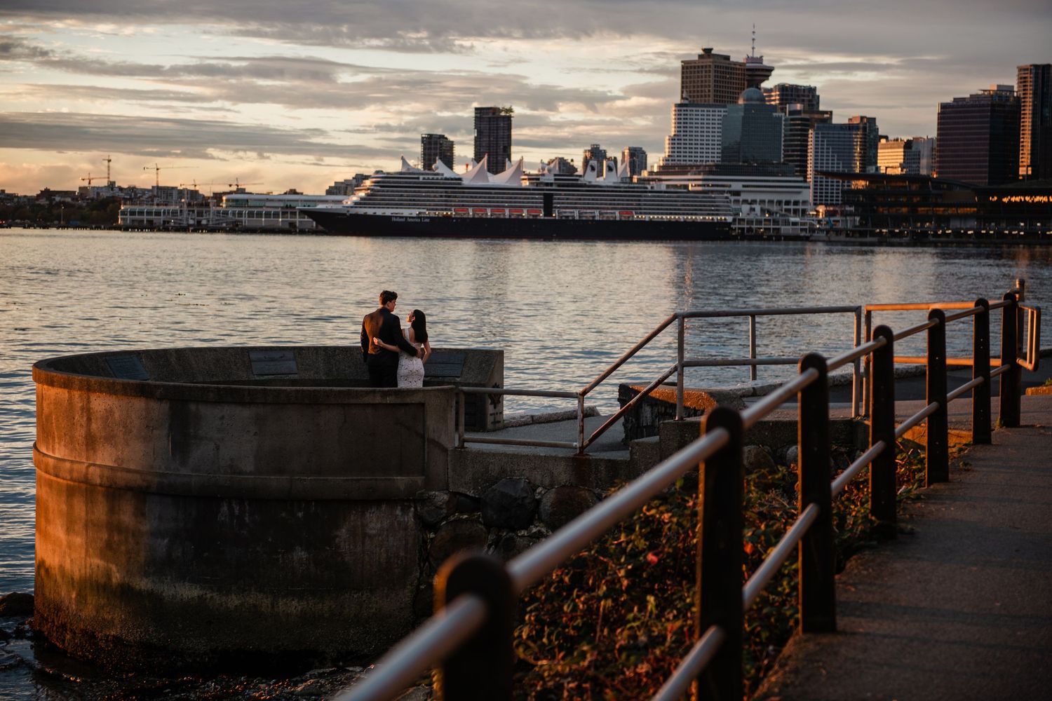 A cruise ship docks at sunset along Vancouver's waterfront with downtown skyscrapers in the background.