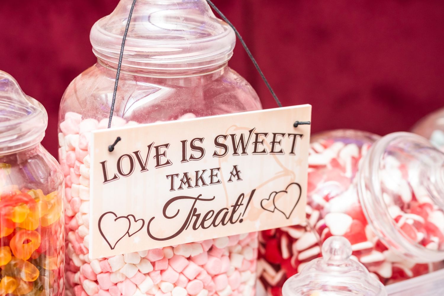 Glass candy jars with 'Love is Sweet' text display at wedding reception.