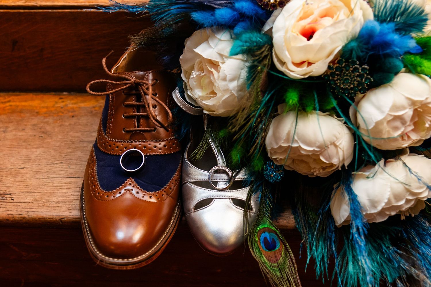 Wedding details featuring leather shoes and blue peacock feather decorations.