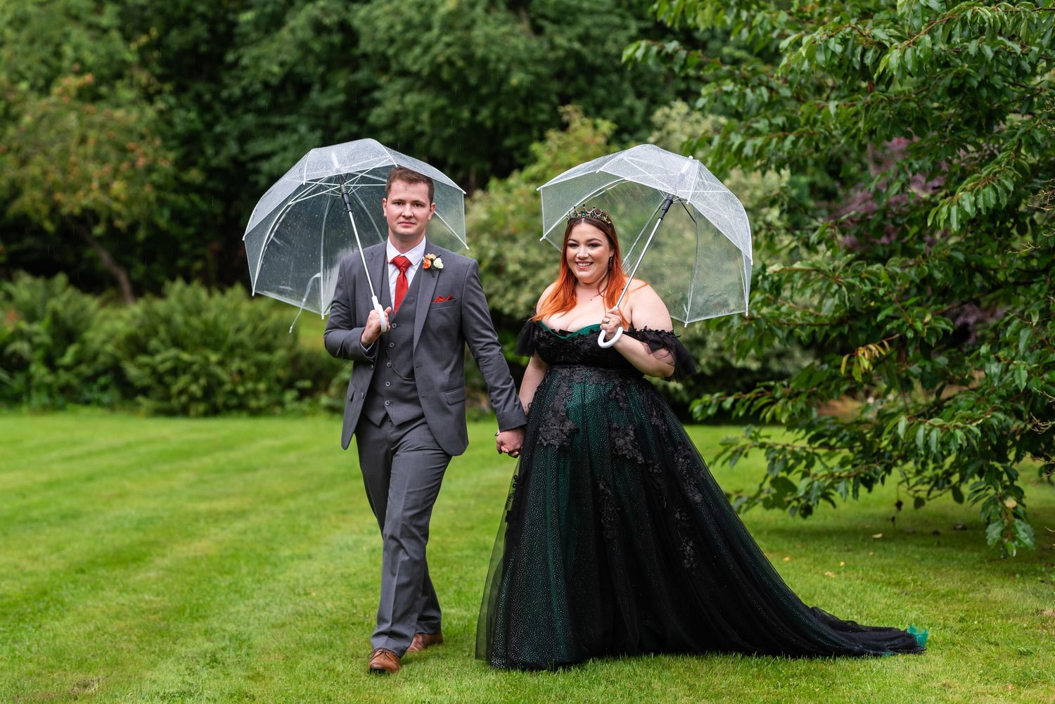 Wedding party walking through a lush green garden setting with umbrellas.