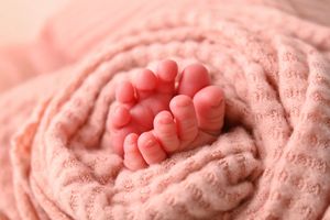 Tiny newborn baby toes peeking out of a soft pink knit blanket wrap in a close-up macro photography shot.