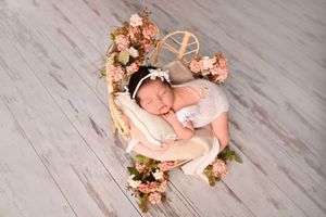Newborn baby girl sleeping peacefully in a heart-shaped wooden bed adorned with pink flowers and a white headband.