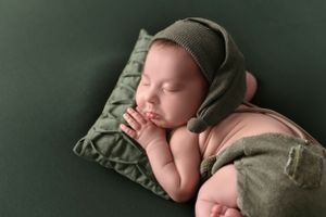 Newborn baby sleeping peacefully on olive green pillow wearing knit bonnet.