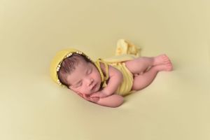 Sleeping newborn baby resting on light yellow background with gentle lighting.