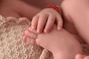 Tiny baby hands and feet resting on textured beige blanket.
