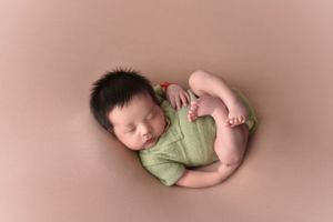 Sleeping newborn photographed on soft pink backdrop with green wrap.